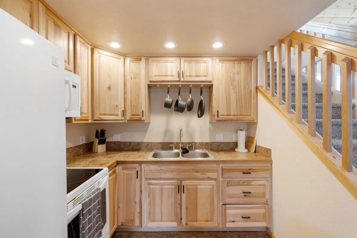 A close-up of the kitchen area highlighting the kitchen sink, hanging pots, and wooden cabinets. Practical elements for meal preparation are front and center, conveying a homey, functional vibe.