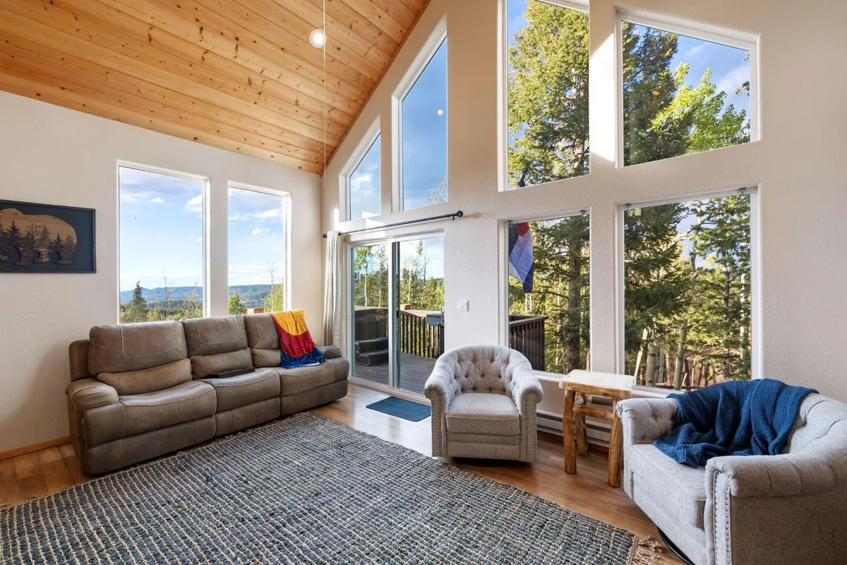 An open-concept living room with a wooden ceiling, expansive windows offering scenic vistas, and a welcoming seating arrangement. The space is designed for gatherings, reading, or simply soaking in the views, fostering togetherness in a tranquil atmosphere.