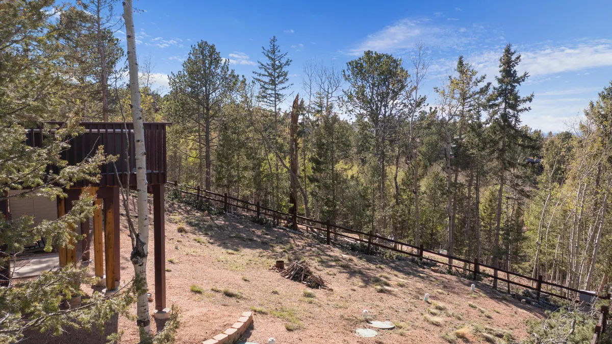A wooden deck overlooks a tree-lined, fenced area, blending seamlessly into the surrounding natural landscape. The setting suggests a relaxing spot for wildlife viewing and enjoying the serenity of the outdoors.