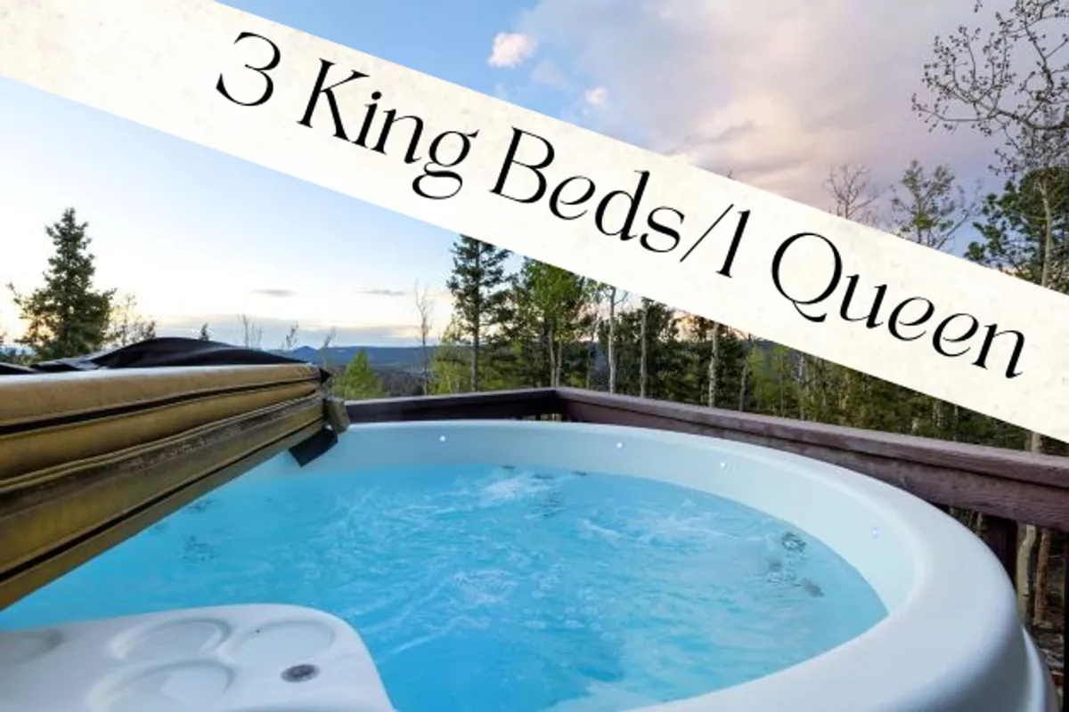 The image shows a sunlit hot tub nestled on a private deck surrounded by towering pines, with sweeping mountain views in the background. The setting is tranquil and inviting, with hints of wildlife-friendly wilderness all around, suggesting peaceful privacy and a deep connection to nature.