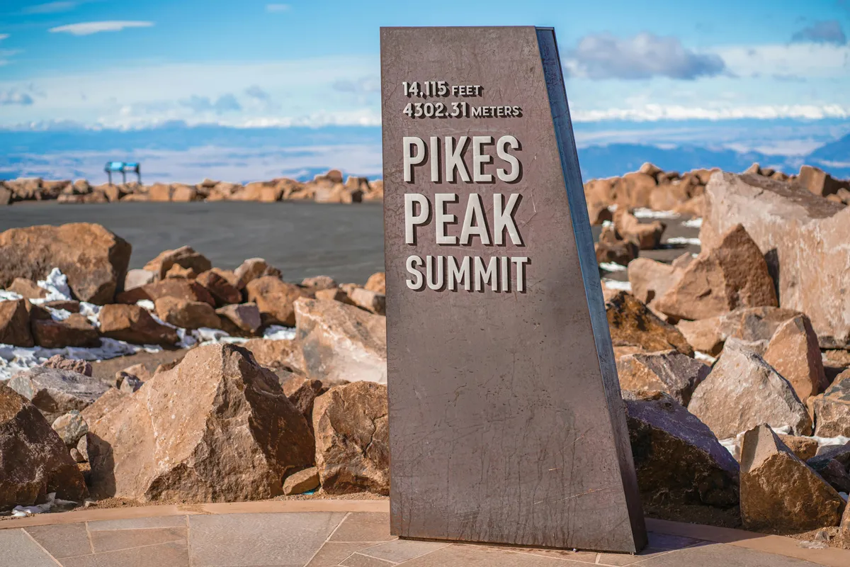 This exterior shot captures the iconic Pikes Peak Summit sign surrounded by rugged rocky terrain and sweeping mountain vistas. It evokes a sense of accomplishment and the grandeur of local outdoor adventures, representing the hiking and exploration opportunities highlighted in the section.
