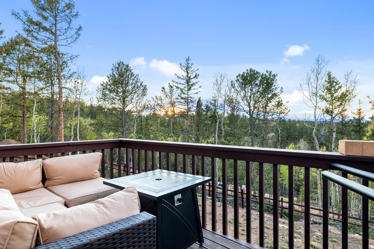 An exterior deck features a comfortable seating area and an outdoor table, perfectly positioned to take in a scenic view of trees and distant mountains. The cozy setup invites relaxation, whether for morning coffee or sunset watching, and seamlessly blends the comfort of the home with the beauty of the outdoors.