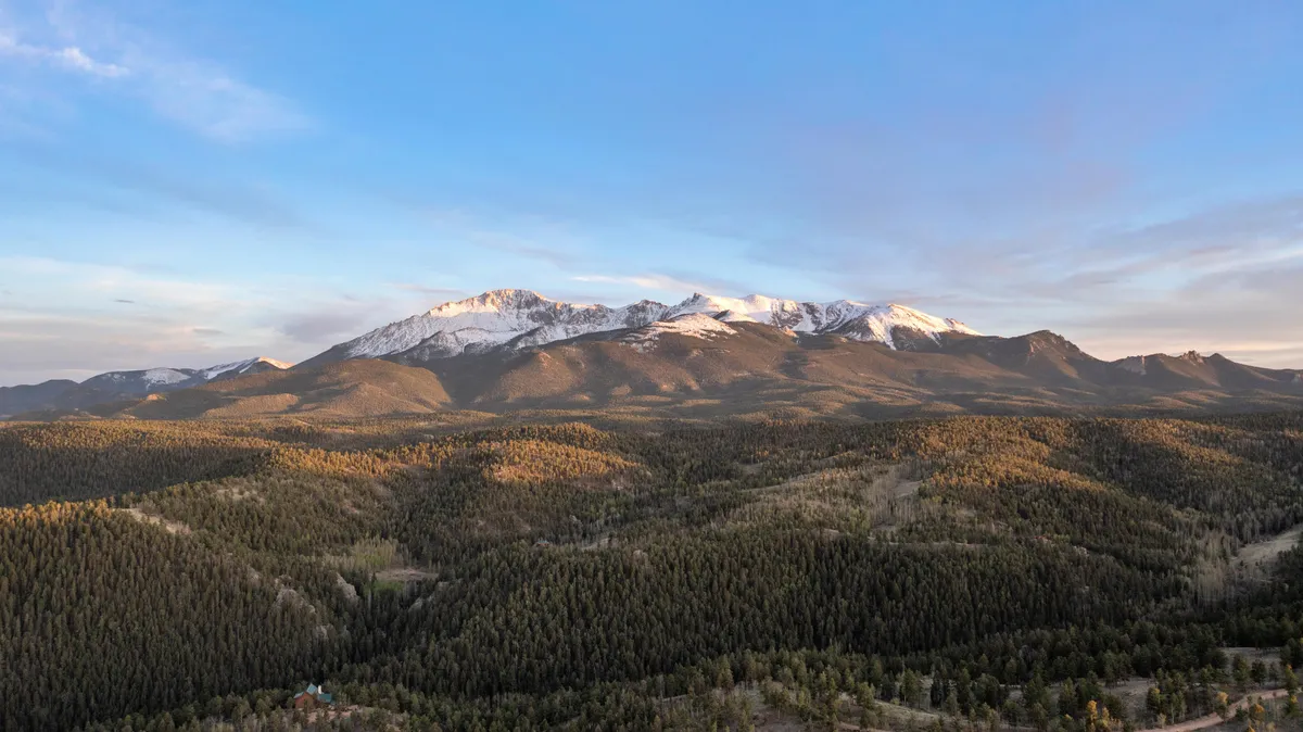 A breathtaking vista of snow-capped mountains and a dense forest stretches beneath an open sky. The landscape is tranquil and expansive, evoking a sense of escape and connection with nature. This perspective emphasizes the magnificent mountain backdrop, reinforcing the promise of scenic views from the property.