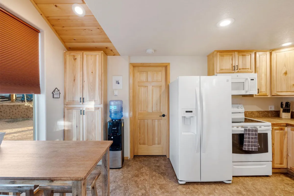 A bright, welcoming kitchen featuring wooden cabinetry, white appliances, and a dining table set for four. The setting exudes warmth, with ample natural light illuminating the inviting space perfect for meal preparation and gathering together.